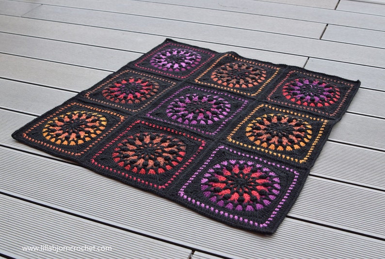 May include: A black crochet blanket with a repeating pattern of colorful circles. The circles are made with a gradient of orange, pink, and purple yarn.