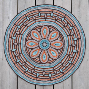 May include: A round crocheted rug with a brown, orange, and blue floral design. The rug has a circular pattern with a central flower and concentric rings of different colors.
