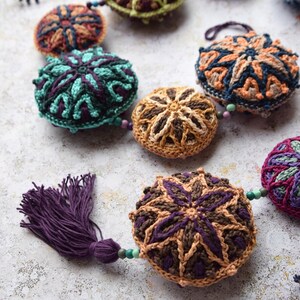 May include: A garland of crocheted round ornaments with intricate geometric patterns in shades of brown, green, blue, and purple. The ornaments are strung together with beads and a purple tassel.