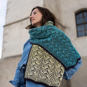 May include: A rectangular knit scarf featuring a two-tone color-blocked design. One section is a vibrant teal with dark navy accents, while the other is a pale yellow with dark navy accents. The scarf has a textured, repeating leaf-like pattern.