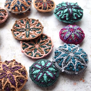 May include: A collection of colourful crocheted coasters with intricate geometric patterns. The coasters are made in various shades of brown, green, blue, and purple.
