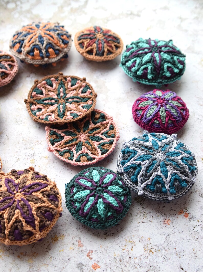 May include: A collection of colourful crocheted coasters with intricate geometric patterns. The coasters are made in various shades of brown, green, blue, and purple.