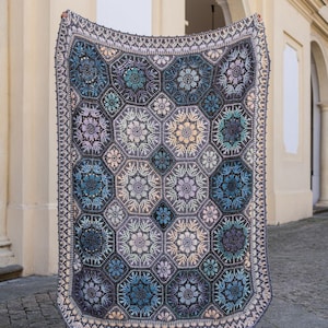 May include: A rectangular crochet blanket featuring a repeating pattern of hexagonal motifs. The design incorporates shades of blue, purple, grey, and cream, with intricate floral-like textures within each hexagon and a decorative border.