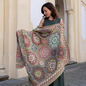 May include: A large, rectangular crochet blanket featuring a complex assembly of hexagonal and floral motifs in shades of sage green, dusty pink, coral, and cream. The intricate needlework displays varied textures and geometric patterns throughout.
