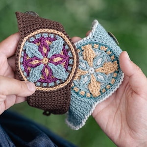 May include: Two crocheted bracelets with floral designs. One bracelet is brown with a purple and blue flower, the other is blue with a yellow and green flower.