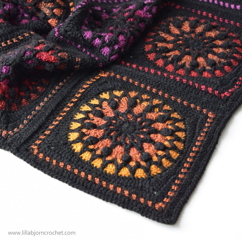 May include: Close-up of a black crochet blanket with a colorful mandala design. The blanket is made with a variety of colors, including red, orange, yellow, and purple. The mandala design is intricate and detailed, and the blanket is soft and cozy.