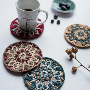 Könnte beinhalten: Vier gehäkelte Untersetzer in verschiedenen Farben und Mustern. Die Untersetzer sind rund und haben ein Mandala-Design. Ein Untersetzer ist rot, weiß und braun. Ein weiterer Untersetzer ist türkis, weiß und braun. Die anderen beiden Untersetzer sind türkis, weiß und braun.