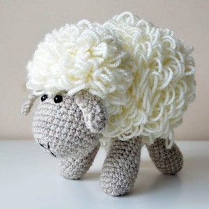 Puede incluir: Un juguete de peluche de oveja blanca de crochet con ojos negros. La oveja tiene un cuerpo de lana blanca esponjosa y una cara y patas grises de crochet.