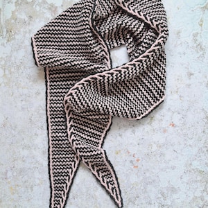 Puede incluir: Bufanda de punto negra y rosa con un patrón de chevrón. La bufanda tiene forma triangular con extremos puntiagudos y un borde rosa. La bufanda está hecha de un material suave y texturizado.