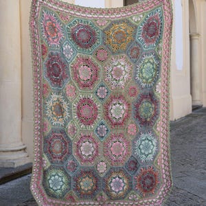 May include: A rectangular crochet blanket featuring a repeating pattern of hexagonal motifs in shades of sage green, dusty pink, mustard yellow, and deep burgundy. The intricate floral designs are joined by green yarn, finished with a decorative border.