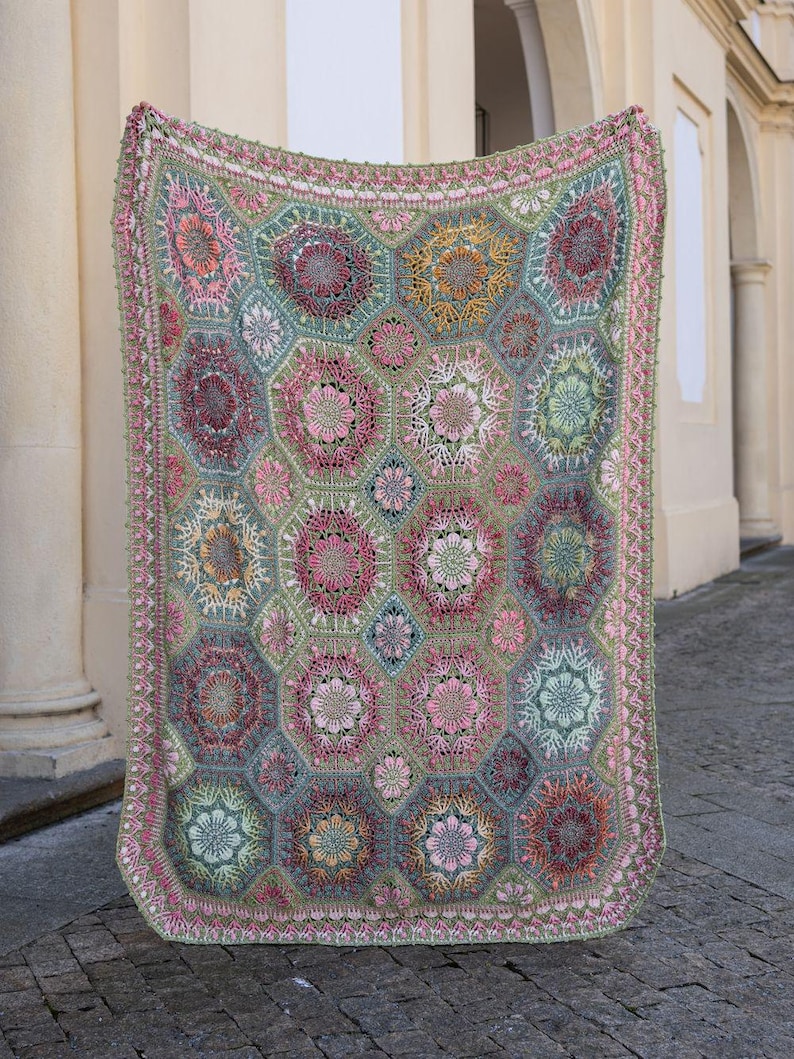 May include: A rectangular crochet blanket featuring a repeating pattern of hexagonal motifs in shades of sage green, dusty pink, mustard yellow, and deep burgundy. The intricate floral designs are joined by green yarn, finished with a decorative border.