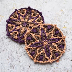May include: Two crocheted coasters with a geometric pattern in shades of brown and purple.