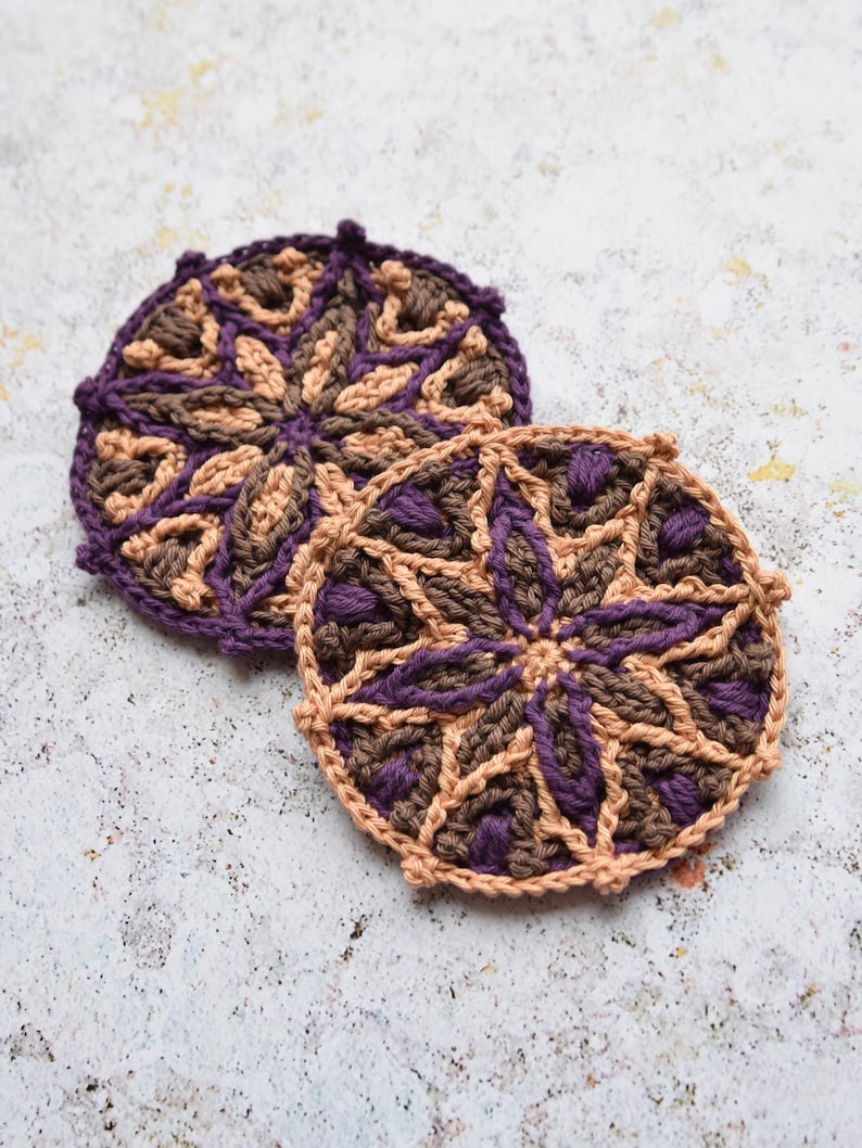 May include: Two crocheted coasters with a geometric pattern in shades of brown and purple.