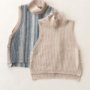 Puede incluir: Dos jerséis sin mangas de cuello alto. Uno tiene un estampado de rayas azul claro y gris, y el otro es de color beige liso. Ambos tienen una textura de punto acanalado y están abotonados en el lateral.