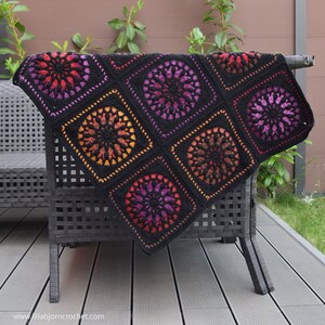 May include: A black crochet throw blanket with a repeating pattern of colorful circles. The blanket is draped over a black wicker chair.