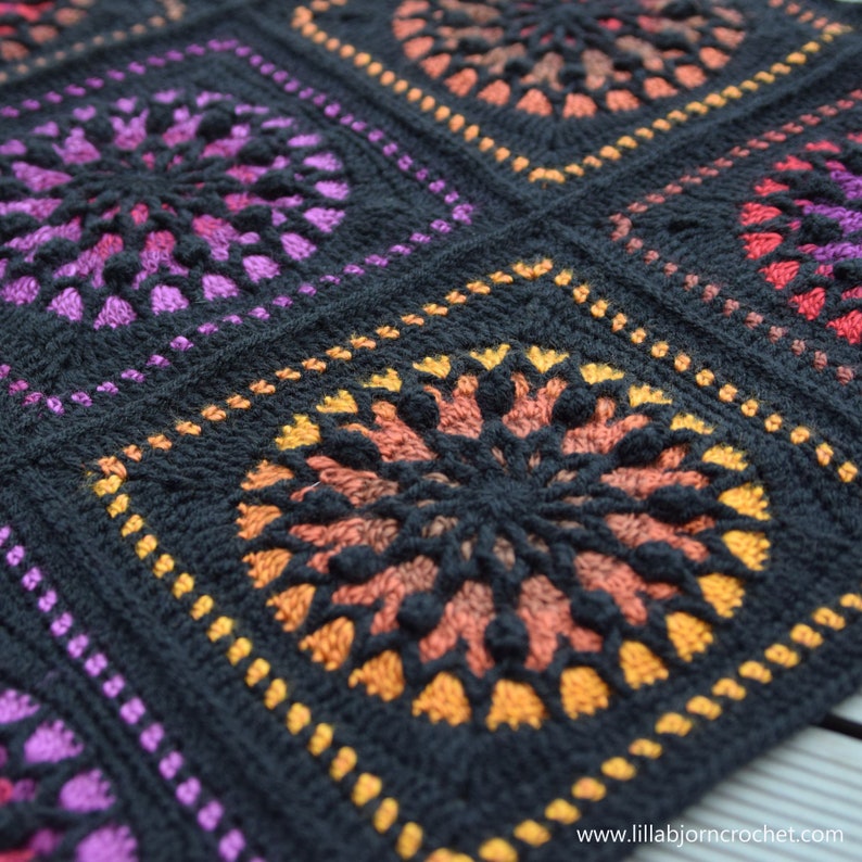 May include: Close-up of a black crochet blanket with colorful circular motifs. The blanket is made with a variety of shades of purple, orange, and yellow yarn.