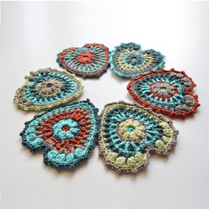 Puede incluir: Seis posavasos de coraz&oacute;n de ganchillo en tonos de turquesa, verde, marr&oacute;n y naranja. Los posavasos est&aacute;n dispuestos en c&iacute;rculo.