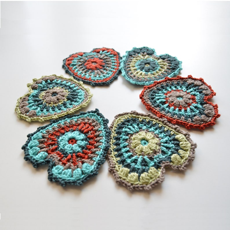 Puede incluir: Seis posavasos de coraz&oacute;n de ganchillo en tonos de turquesa, verde, marr&oacute;n y naranja. Los posavasos est&aacute;n dispuestos en c&iacute;rculo.