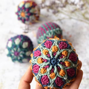 May include: A set of four crocheted ornaments featuring intricate floral designs in shades of pink, orange, green, and blue. The ornaments are embellished with small white beads.