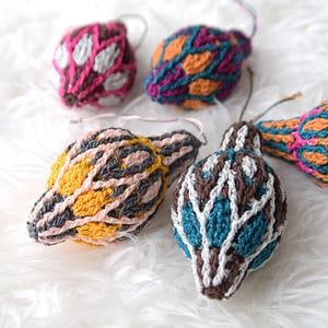 May include: A collection of handmade, colorful, crocheted ornaments. The ornaments feature various patterns and color combinations, including pink, orange, blue, yellow, and brown. Each ornament has a loop for hanging.