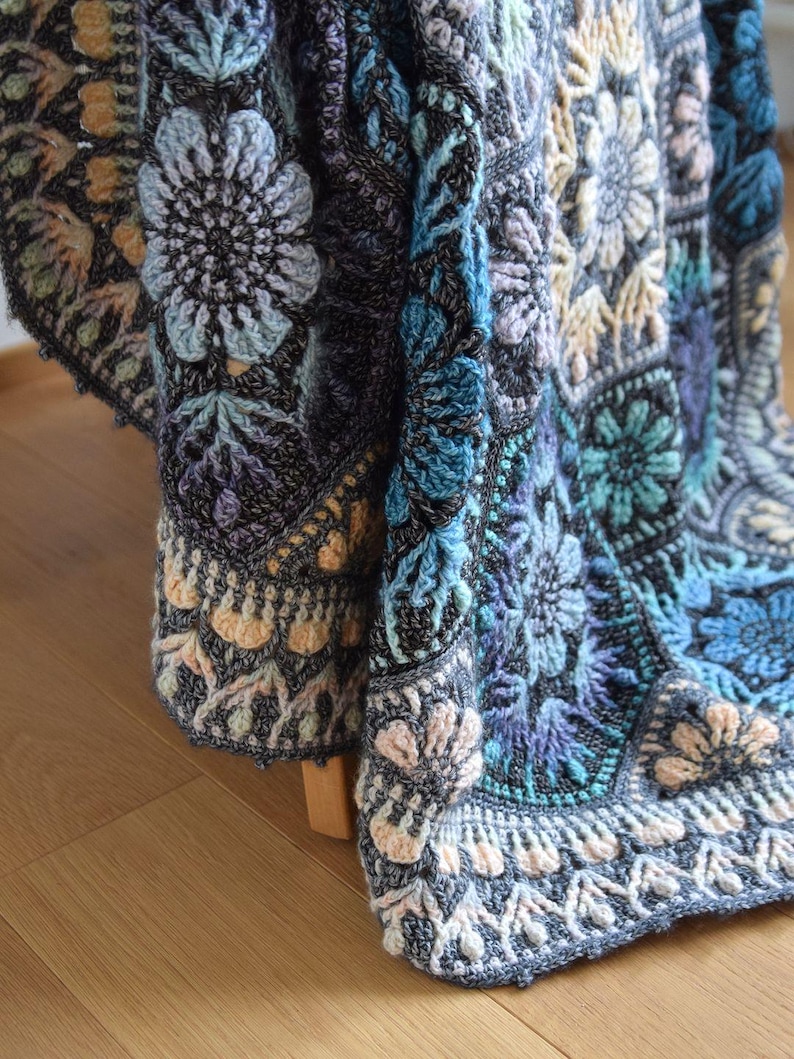 May include: A crochet blanket featuring a complex arrangement of hexagonal motifs in shades of charcoal gray, light blue, teal, and soft peach. The design incorporates intricate floral patterns with raised textures and detailed stitching throughout.
