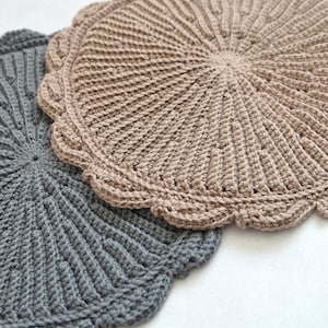 Puede incluir: Dos tapetes de ganchillo circulares con un patrón radial texturizado y un borde festoneado. Un tapete es de color tostado claro y el otro es de color gris oscuro. Ambos artículos están elaborados con un patrón de punto denso desde el centro.