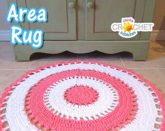 May include: A handmade, circular area rug in a spiral design. The rug features alternating bands of white and coral pink, with a scalloped edge. The words "Area Rug" are in a blue bubble font. The rug is placed on a tiled floor.