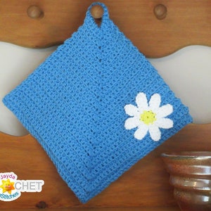 May include: A blue crocheted pot holder with a white daisy flower appliqué. The pot holder is hanging on a wooden shelf with two brown ceramic mugs.