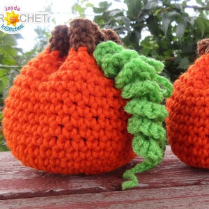 May include: Two crocheted orange pumpkin-shaped drawstring bags with green crocheted stems. The bags are sitting on a wooden surface.