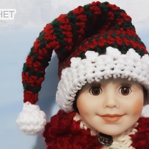 May include: A red and green crocheted elf hat with a white pom-pom on the end of the pointy tip. The hat is on a doll's head.
