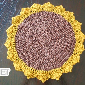 Op de afbeelding: Een gehaakte zonnebloemonderzetter met een bruin centrum en een gele buitenring. De onderzetter is gemaakt met een textuur-steek en heeft een gegolfde rand.