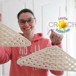 May include: Two crocheted white hangers with a wire hook. The hangers are in the shape of a triangle with a lattice pattern. The hangers are being held by a person wearing a pink hoodie.
