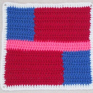 May include: A crochet blanket square with a white border, featuring a red, pink, and blue color scheme. The square is made up of four smaller squares, each a different color. The text "Blanket Square" is visible in the image.