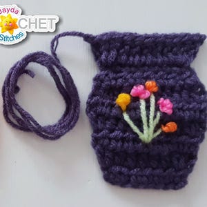 May include: Crocheted vase-shaped ornaments in orange and purple. The orange vase has white flecks. The purple vase features embroidered flowers. A purple yarn is also included. The logo "Jayda Crochet in Stitches" is in the top right.