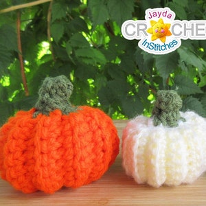 May include: Three crocheted pumpkins in orange, white, and gray. The pumpkins are sitting on a wooden surface. The pumpkins are all about 4 inches tall.