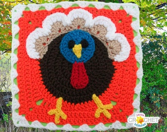 Puede incluir: Un cuadrado tejido a crochet con un diseño de pavo colorido. El pavo es marrón con una papada roja, cabeza azul, pico amarillo y plumas blancas. El cuadrado está rodeado por un borde verde y blanco.