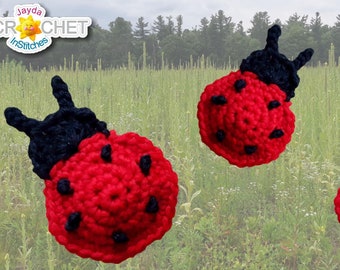 May include: Three crocheted ladybugs with red bodies, black spots, and black heads. The ladybugs are against a blurred background of green grass.
