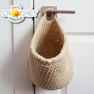 May include: A beige crocheted hanging basket with a loop at the top. The basket is hanging on a white door.