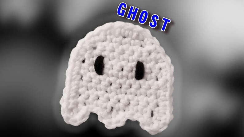 May include: White crocheted ghost with black eyes. The ghost is a handmade craft item. The word "GHOST" is written in blue letters above the ghost.