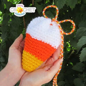 May include: A crocheted candy corn shaped pouch with a white top, orange middle, and yellow bottom. The pouch has a white and orange string attached to it.