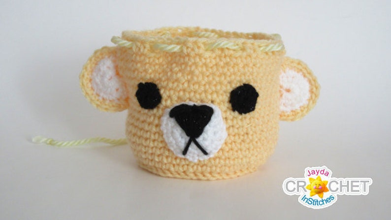 May include: A crocheted yellow bear-shaped basket with black eyes, a white nose, and a white mouth. The basket is lined with a yellow yarn.