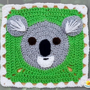 May include: A crocheted square featuring a koala bear face in grey, white, and black yarn. The koala is surrounded by green crocheted leaves. The square has a white crocheted border with a scalloped edge.