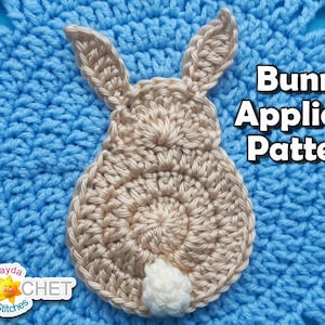 May include: A crocheted bunny applique pattern with a light blue background. The bunny is beige with a white tail.