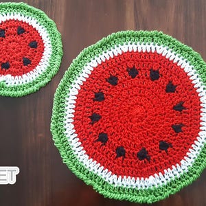 Puede incluir: Dos posavasos de sandía hechos a mano con ganchillo. Los posavasos presentan un centro rojo con detalles de semillas negras, un anillo blanco en el medio y un anillo exterior verde. Sobre una superficie de madera marrón oscuro. El logotipo "Jayda Crochet InStitches" está abajo a la izquierda.
