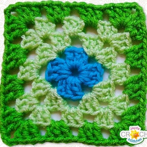 May include: A green and light green crochet square with a blue flower in the center. The square has a border of green crochet.