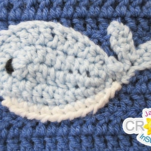 May include: A crocheted whale applique in light blue and white, with a black eye, on a blue crocheted background. The text "Jayda Crochet InStitches" is visible in the bottom right corner.