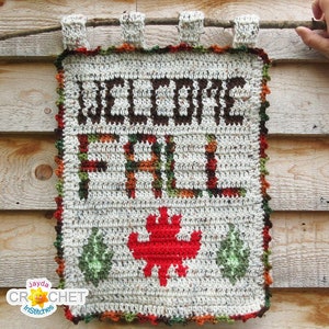 May include: A crocheted welcome sign with the words "Welcome Fall" in brown yarn and a red crocheted maple leaf. The sign is hanging on a wooden wall.