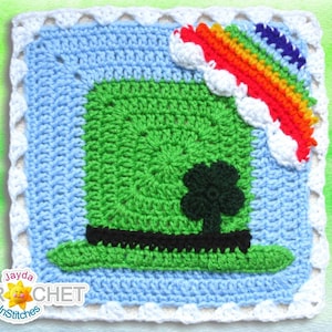 Può includere: Un quadrato all'uncinetto con un cappello da folletto verde con una fascia nera e un trifoglio, un arcobaleno con nuvole bianche e uno sfondo di cielo blu.
