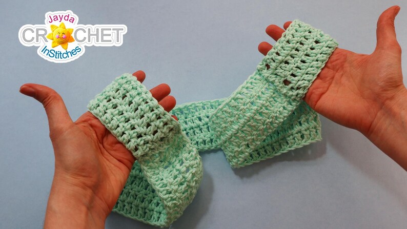 May include: A light green crocheted headband, held in two hands. The headband is made with a simple stitch pattern and has a slightly textured look.