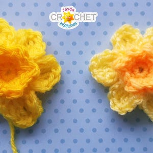 May include: Two crocheted daffodil flowers, one yellow and one with a yellow outer layer and an orange center. The flowers are on a blue background with white polka dots.